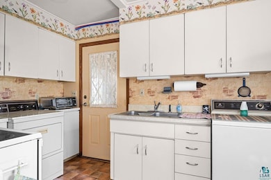Kitchen featuring a sink, backsplash, light countertops, and white cabinetry