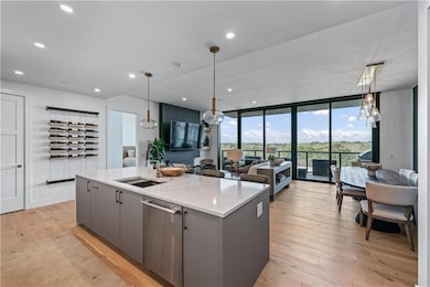 Kitchen with gray cabinetry, a center island with sink, stainless steel dishwasher, light wood-style floors, and open floor plan