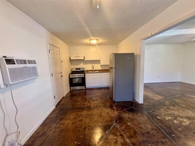 Kitchen with white cabinetry, appliances with stainless steel finishes, a textured ceiling, a wall mounted air conditioner, and concrete flooring