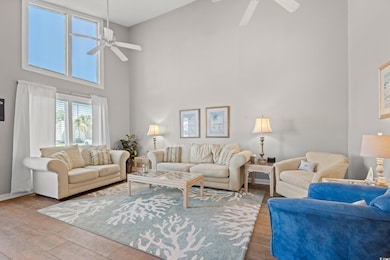 Living area with ceiling fan, a towering ceiling, and wood finished floors