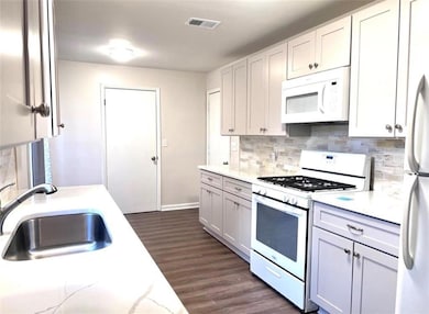 Kitchen featuring white appliances, dark wood finished floors, tasteful backsplash, light stone countertops, and white cabinetry