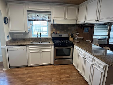 Kitchen featuring dishwasher, stainless steel gas stove, ventilation hood, and wood finished floors