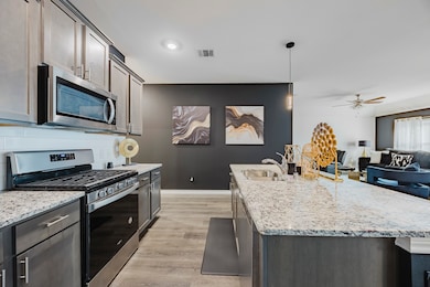 Kitchen with appliances with stainless steel finishes, light stone counters, light wood-type flooring, a ceiling fan, and open floor plan