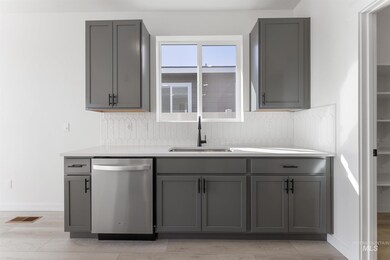 Kitchen with gray cabinetry, dishwasher, light wood-style floors, and light stone counters