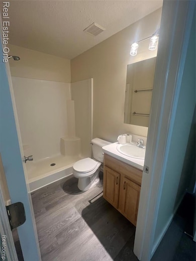 Bathroom with wood finished floors, a shower stall, vanity, and a textured ceiling