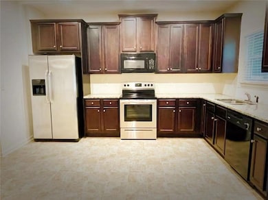 Kitchen with black appliances, dark brown cabinets, and light stone countertops