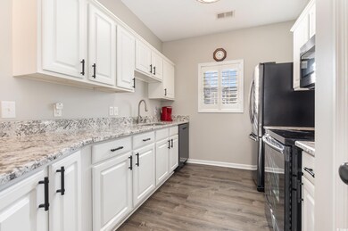 Kitchen featuring visible vents, range with electric cooktop, a sink, stainless steel microwave, and white cabinetry