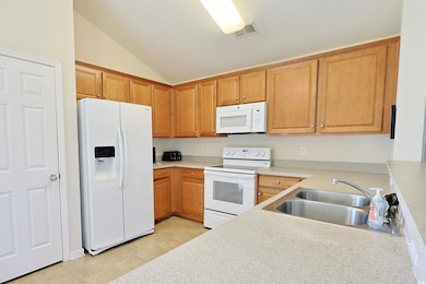 Kitchen featuring white appliances, vaulted ceiling, and light countertops