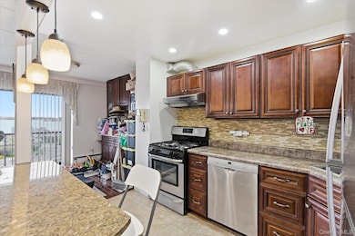 Kitchen featuring appliances with stainless steel finishes, hanging light fixtures, tasteful backsplash, light tile patterned floors, and recessed lighting