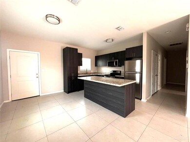 Kitchen featuring stainless steel appliances, a center island, light tile patterned flooring, dark cabinetry, and light stone countertops