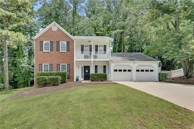 View of front of house featuring a garage, driveway, brick siding, a balcony, and view of scattered trees