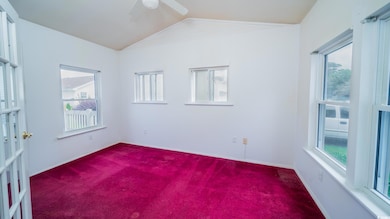 Empty room with dark carpet, vaulted ceiling, a ceiling fan, and baseboards