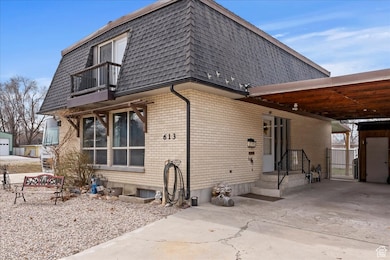 Back of house with a balcony, a gate, concrete driveway, an attached carport, and mansard roof