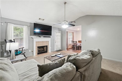 Carpeted living room featuring vaulted ceiling, a tiled fireplace, and ceiling fan