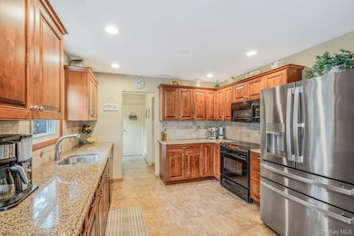 Kitchen featuring black appliances, tasteful backsplash, brown cabinetry, light stone countertops, and recessed lighting