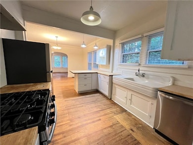 Kitchen with stainless steel appliances, a peninsula, light wood finished floors, decorative light fixtures, and white cabinetry