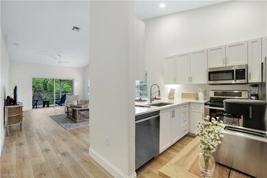 Kitchen featuring appliances with stainless steel finishes, a sink, a towering ceiling, light wood-style floors, and tasteful backsplash