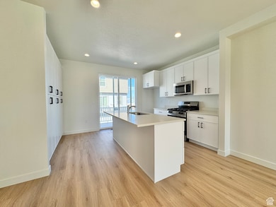 Kitchen featuring appliances with stainless steel finishes, white cabinets, a center island with sink, recessed lighting, and light wood finished floors
