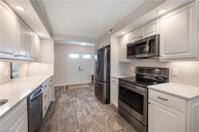 Kitchen with appliances with stainless steel finishes, white cabinetry, crown molding, recessed lighting, and light stone countertops