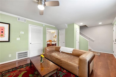 Living area featuring wood finished floors, crown molding, a ceiling fan, stairway, and recessed lighting