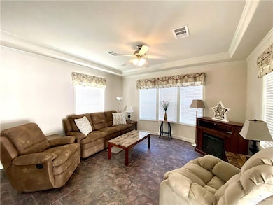 Living area featuring a ceiling fan, crown molding, a raised ceiling, and a fireplace