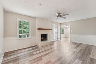 Unfurnished living room with a wainscoted wall, ceiling fan, a textured ceiling, a brick fireplace, and wood finished floors