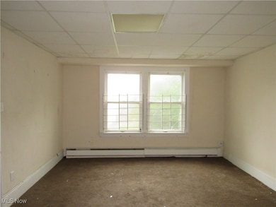 Empty room with a drop ceiling and a baseboard heating unit