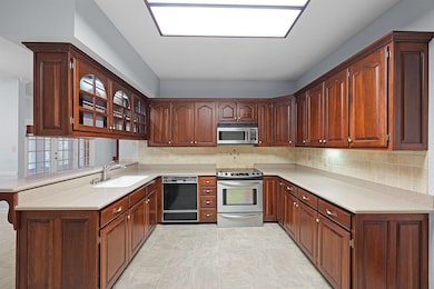 Kitchen featuring stainless steel appliances, a peninsula, light countertops, backsplash, and glass insert cabinets