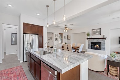 Kitchen featuring hanging light fixtures, appliances with stainless steel finishes, light stone countertops, a ceiling fan, and a fireplace