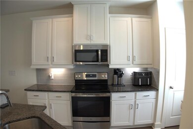 Kitchen featuring stainless steel appliances, a sink, decorative backsplash, white cabinetry, and dark stone counters