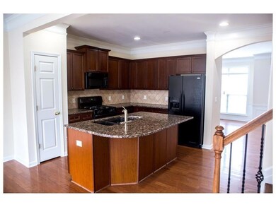 Kitchen featuring black appliances, a sink, dark wood-type flooring, arched walkways, and dark stone countertops