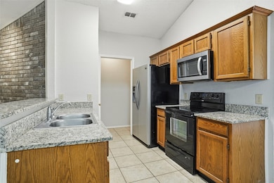 Kitchen featuring electric range, stainless steel microwave, a textured ceiling, light tile patterned floors, and brown cabinets