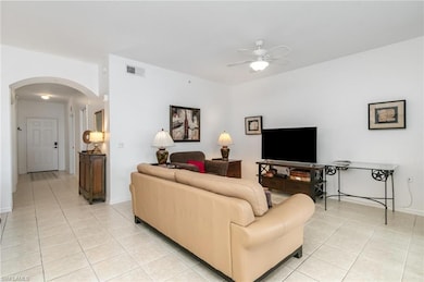 Living room featuring arched walkways, light tile patterned floors, a ceiling fan, and baseboards