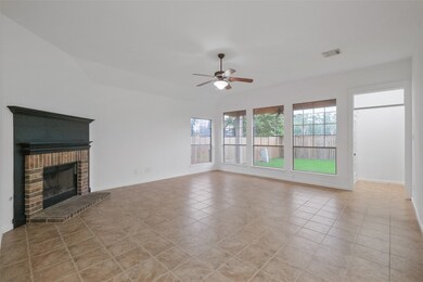 View of the spacious, well-lit living room with a tiled floor, featuring a classic fireplace and ample natural light from large windows and a glass door leading to the backyard.