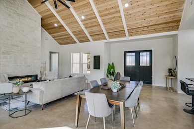 Dining area with high vaulted ceiling, a wooden ceiling with exposed beams, a fireplace, concrete floors, and recessed lighting