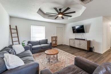 Living room featuring ceiling fan, a tray ceiling, and dark wood-type flooring