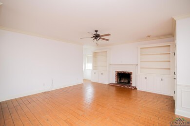 Unfurnished living room featuring built in features, ceiling fan, crown molding, and a brick fireplace
