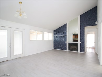 Unfurnished living room with a wealth of natural light, a fireplace, wood finished floors, and a notable chandelier