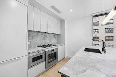 Kitchen featuring modern cabinets, appliances with stainless steel finishes, tasteful backsplash, white cabinets, and light stone counters