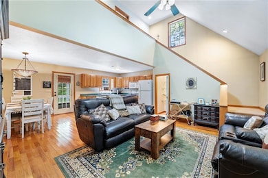 Living area with ceiling fan, plenty of natural light, light wood-style floors, and high vaulted ceiling