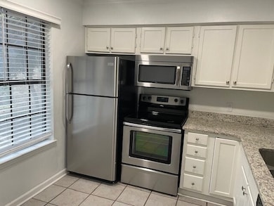 Kitchen with stainless steel appliances, white cabinets, light stone counters, and light tile patterned floors