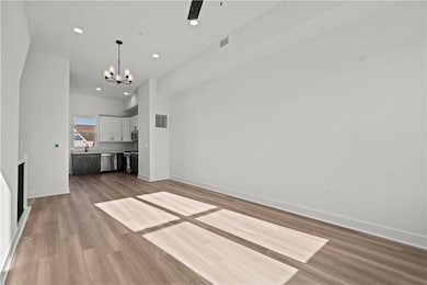 Unfurnished living room with sink, ceiling fan with notable chandelier, and light hardwood / wood-style floors