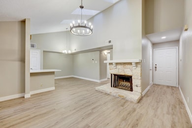 Unfurnished living room featuring high vaulted ceiling, a fireplace, light wood-style flooring, and a chandelier