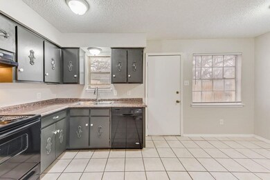 Kitchen featuring black appliances, dark countertops, a textured ceiling, plenty of natural light, and light tile patterned floors