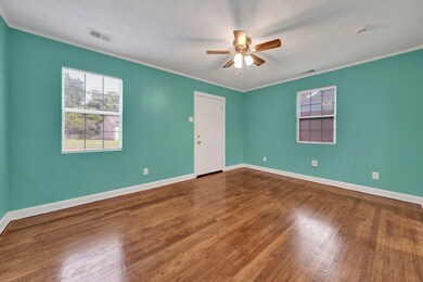 Empty room featuring healthy amount of natural light, a ceiling fan, dark wood-style flooring, and crown molding