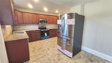 Kitchen featuring appliances with stainless steel finishes, light stone counters, decorative backsplash, and light tile patterned floors