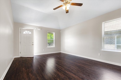 Spare room featuring dark wood-type flooring, ceiling fan, lofted ceiling, and baseboards