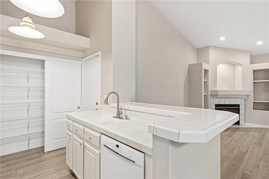 Kitchen with tile counters, light wood finished floors, dishwasher, built in features, and recessed lighting