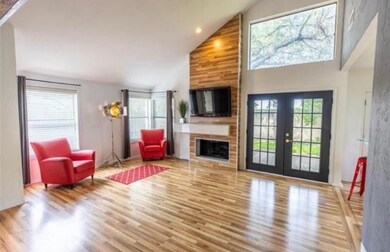 Living room with a large fireplace, high vaulted ceiling, french doors, and wood finished floors