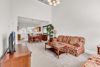 Living area with a chandelier, light carpet, baseboards, and a towering ceiling